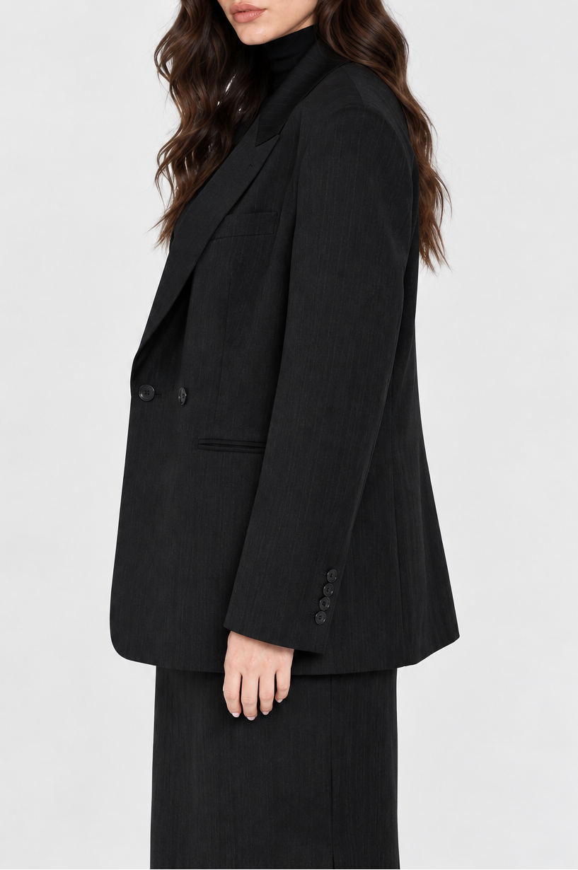 A woman modeling a black double-breasted blazer with a black turtleneck underneath, shown from a side profile against a light gray studio background.