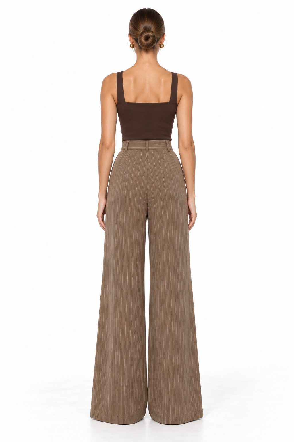 A woman viewed from the back wearing a dark brown square-neck top and high-waisted, wide-leg taupe-brown pleated trousers against a plain white studio background.